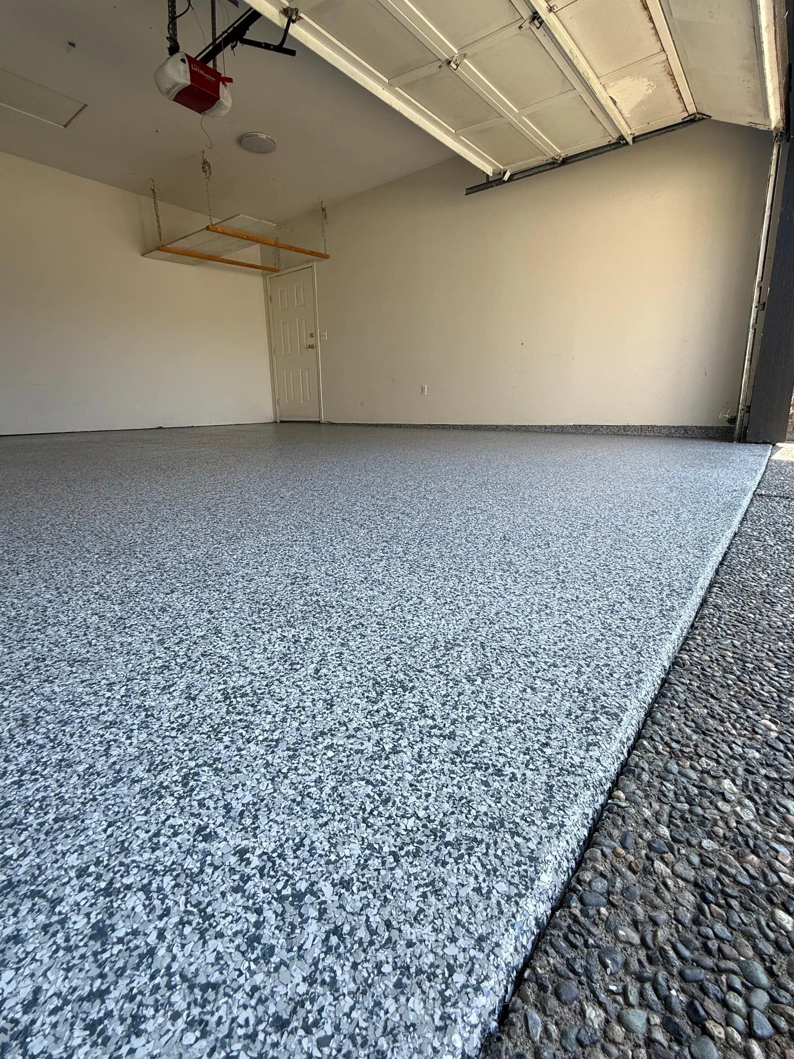 Single garage with a light grey and white flake floor meeting an exposed aggregate driveway at the threshold